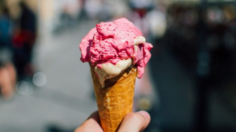 Hand holding a melting waffle cone with pink and vanilla ice cream on a sunny day