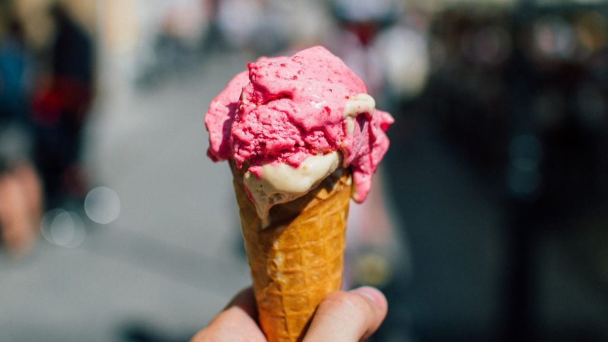 Hand holding a melting waffle cone with pink and vanilla ice cream on a sunny day