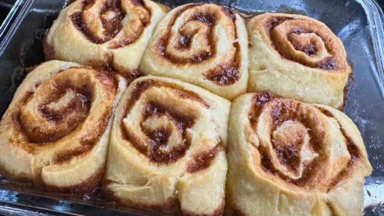 Freshly baked sourdough cinnamon rolls in a glass pan with golden, gooey swirls