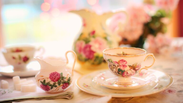 Vintage floral tea cup and creamer set on a lace tablecloth with soft pink decor