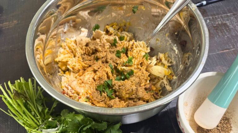 Mixing bowl filled with seasoned shredded chicken, herbs, and cheese on a dark wood table
