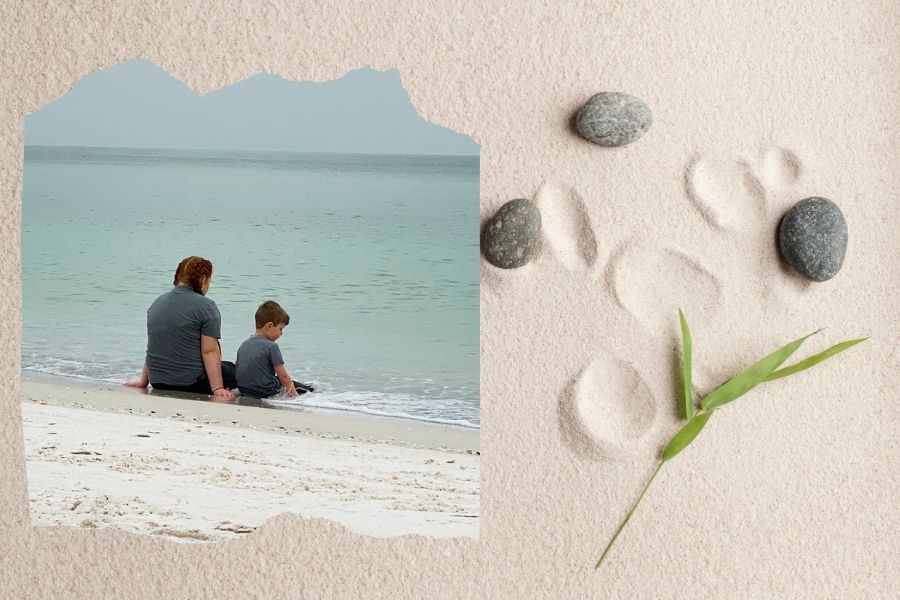 Two children sitting quietly by the edge of the ocean, facing the calm sea on a peaceful beach.