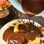 Chocolate gravy being poured over biscuits on a fall-themed plate