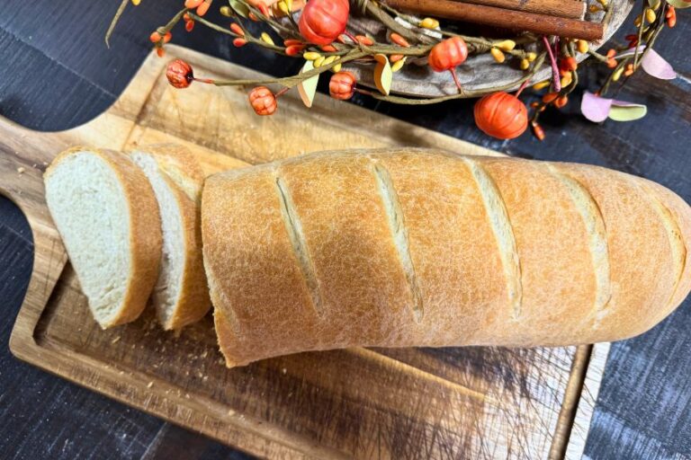 Golden loaf of homemade French bread with slices cut on a wooden cutting board