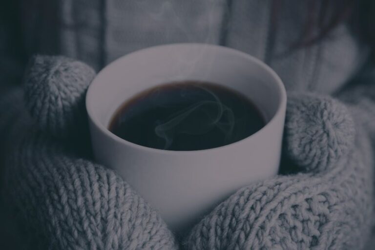A steaming mug held in gray knit gloves, radiating warmth and comfort on a cold day.