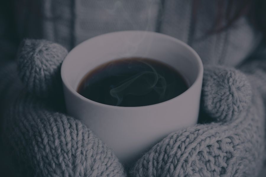 A steaming mug held in gray knit gloves, radiating warmth and comfort on a cold day.
