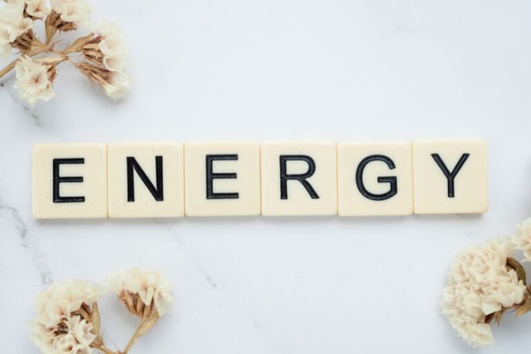 Letter tiles spelling out “ENERGY” on a white marble surface, surrounded by dried white flowers.
