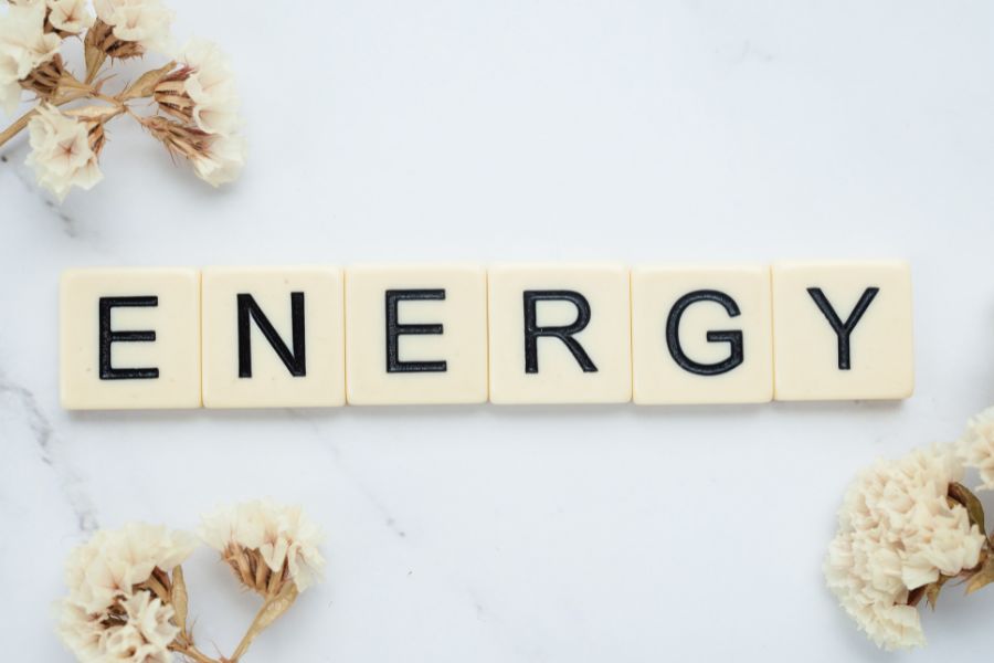Letter tiles spelling out “ENERGY” on a white marble surface, surrounded by dried white flowers.