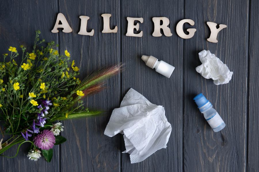 Flat lay of allergy relief items with flowers, tissues, and nasal sprays on dark wood, representing seasonal allergies.