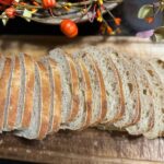 Freshly sliced sourdough bread on a wooden cutting board with fall decor in the background.