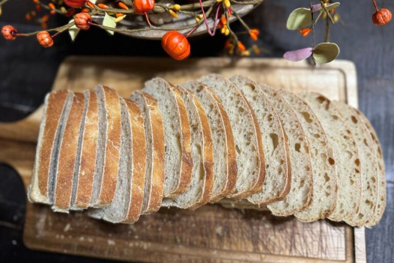 Freshly sliced sourdough bread on a wooden cutting board with fall decor in the background.