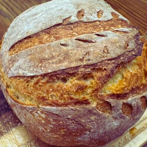 Crusty loaf of no-knead rustic bread on a wooden cutting board