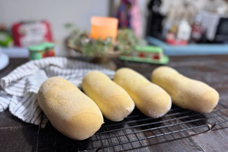 Homemade sub sandwich rolls cooling on a wire rack with a cozy kitchen background