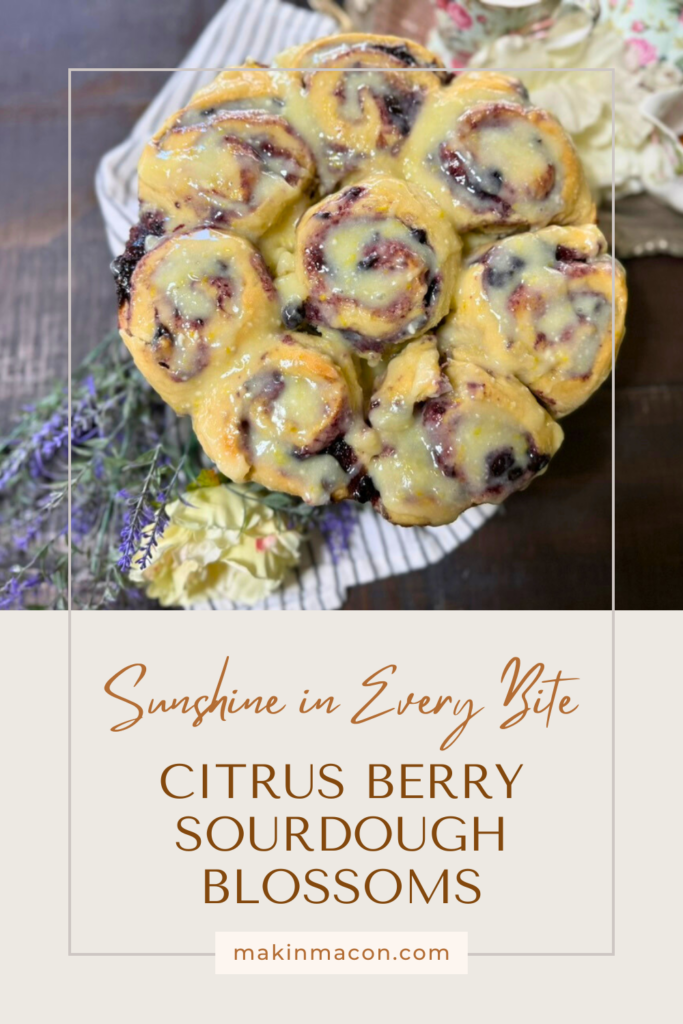 Overhead view of glazed citrus berry sourdough blossoms on a wooden table with flowers, with text overlay reading "Sunshine in Every Bite – Citrus Berry Sourdough Blossoms."