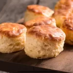Flaky sourdough biscuits stacked on a rustic wooden board, golden brown and fresh from the oven