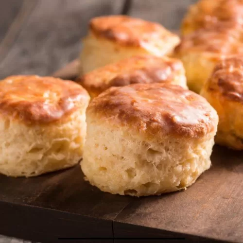 Flaky sourdough biscuits stacked on a rustic wooden board, golden brown and fresh from the oven
