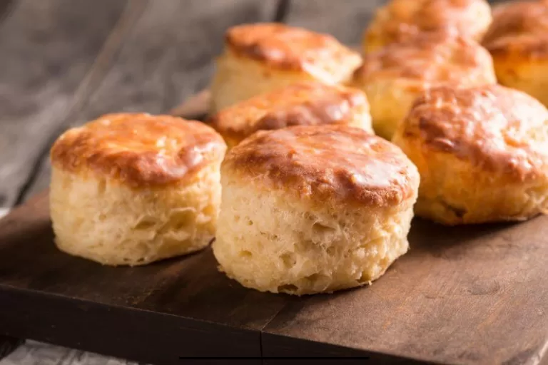 Flaky sourdough biscuits stacked on a rustic wooden board, golden brown and fresh from the oven