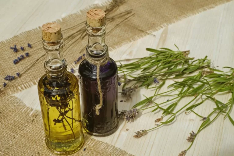 Two corked glass bottles of essential oils beside fresh lavender on a rustic wood table — Stress Be-Gone blend banner