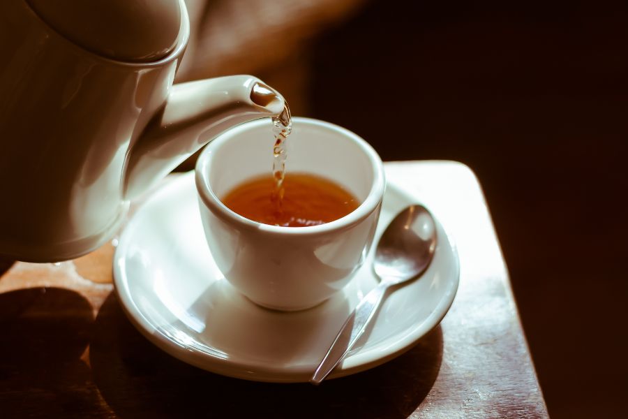 Warm tea being poured into a cup representing a soothing essential oil blend for sore throat relief