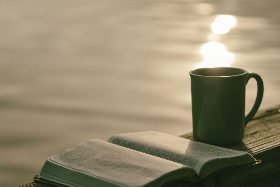 Open Bible and coffee by the water representing finding strength in weakness through faith