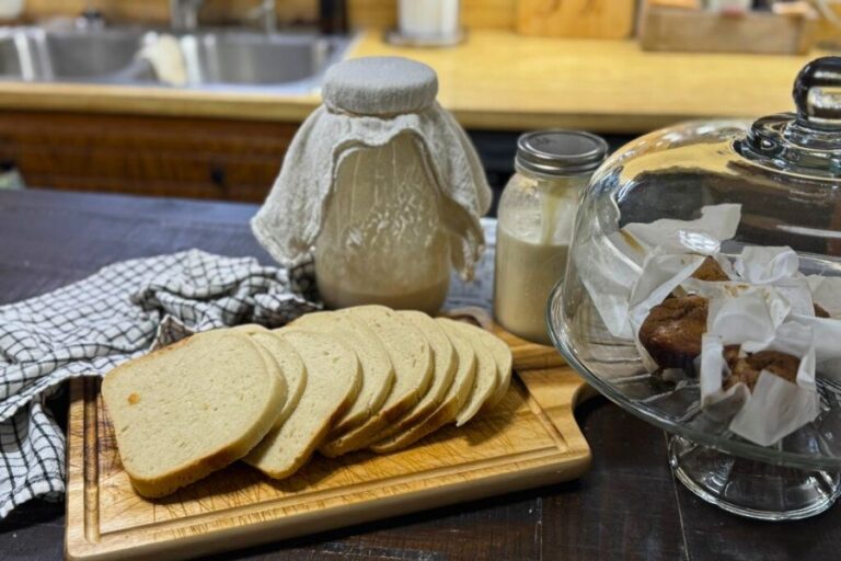 Sliced sourdough bread on a wooden board with sourdough starter, milk, and baked goods in a spring kitchen setting