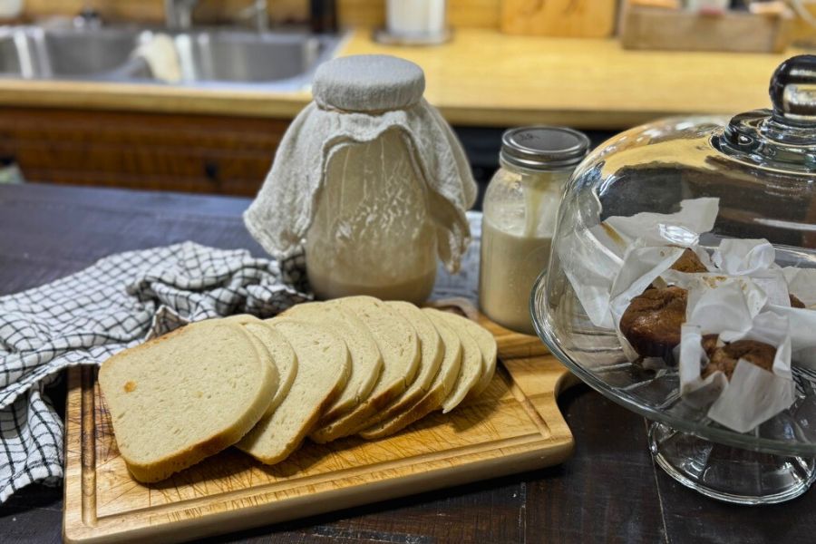 Sliced sourdough bread on a wooden board with sourdough starter, milk, and baked goods in a spring kitchen setting