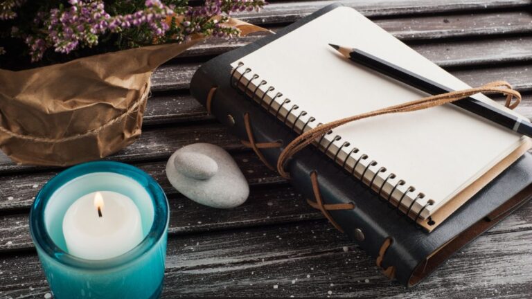 A peaceful journal scene with a candle and flowers—capturing the quiet beauty of slowing down and creating space for rest and reflection.