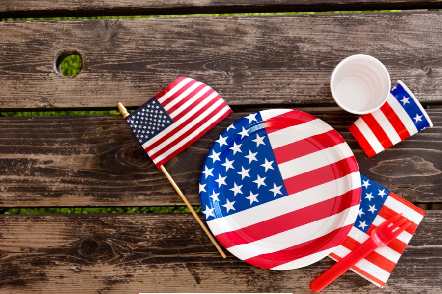 Patriotic table setting with American flag-themed paper plate, cup, and napkin on a rustic picnic table