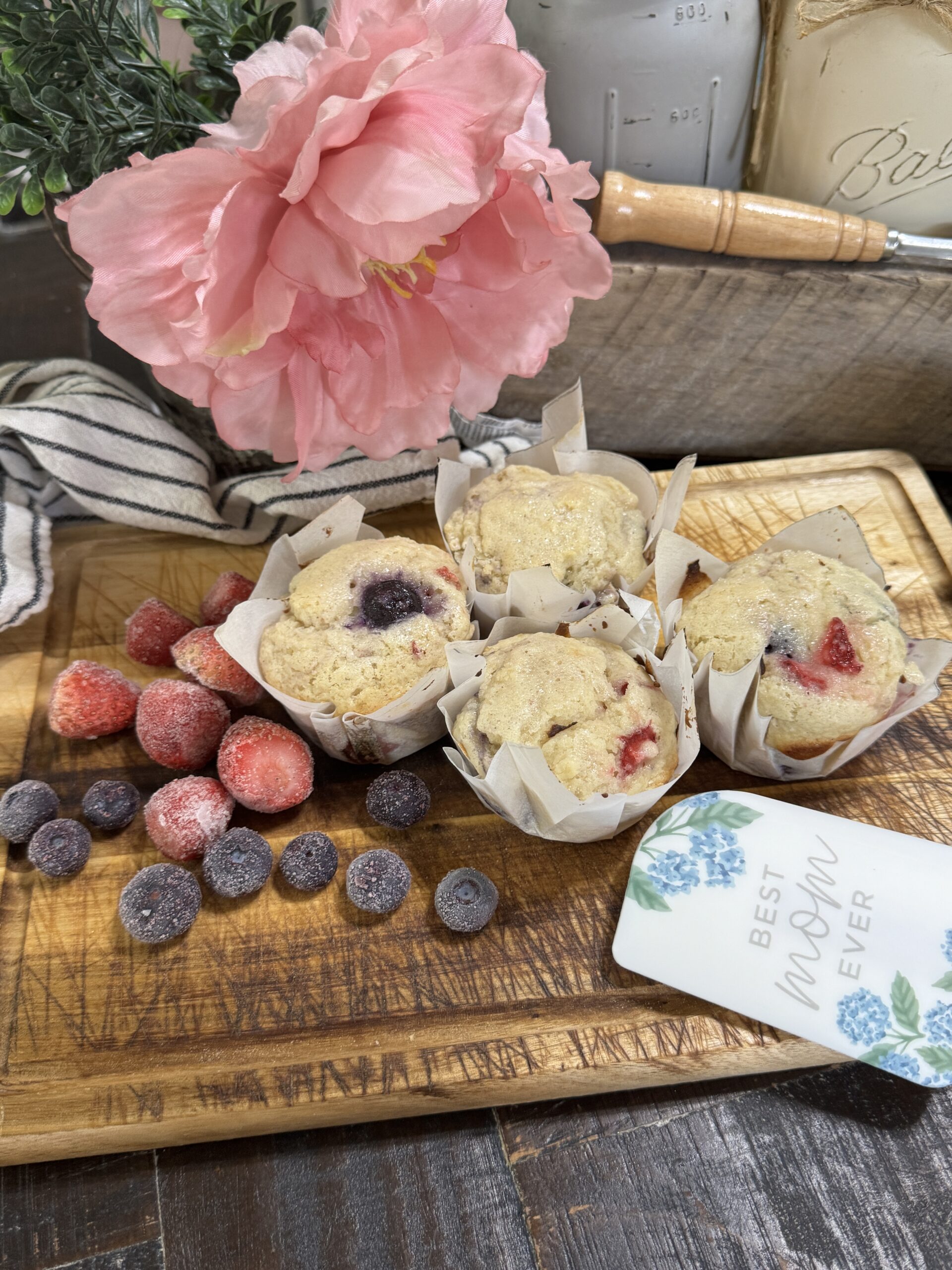 Sourdough blueberry and strawberry muffins on a wooden board surrounded with florals and strawberries and blueberries.