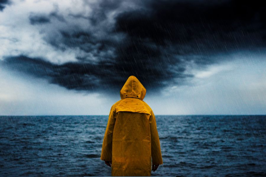 Person in a yellow raincoat standing alone in the rain, facing a stormy ocean