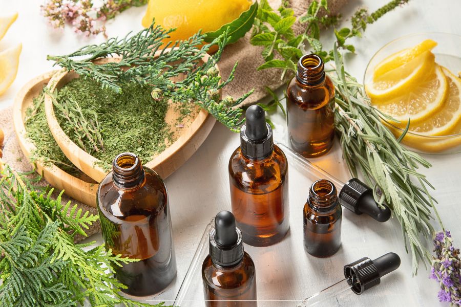 Essential oil bottles surrounded by herbs, lemon slices, and greenery on a white background
