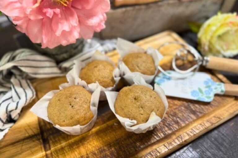 Homemade sourdough banana muffins in parchment liners on a wooden tray with flowers in the background