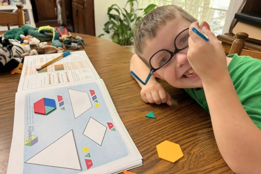 Smiling boy doing homeschool math with shape blocks and workbook during his first year homeschooling