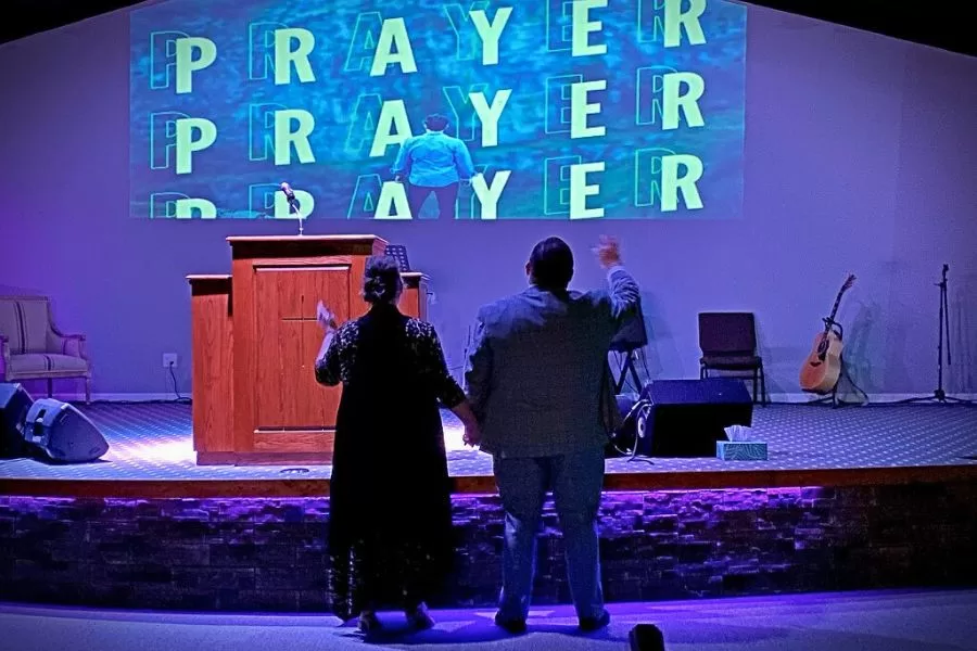 Couple holding hands at the altar during prayer, symbolizing unity and encouragement for the weary in spiritual warfare.