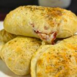 Homemade pizza pockets on a floral plate, filled with mozzarella, pepperoni, and pizza sauce, topped with parmesan and herbs
