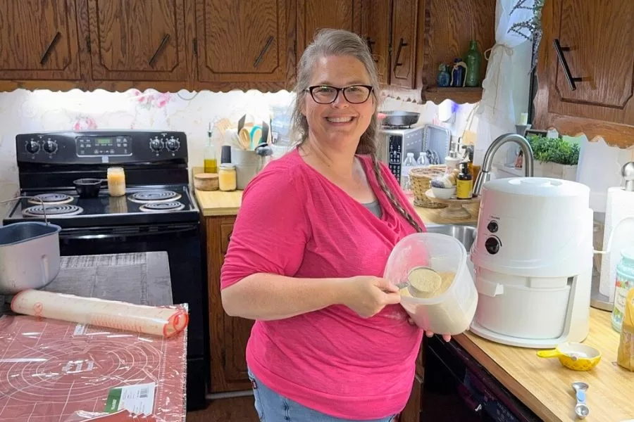 Woman smiling in kitchen while scooping freshly milled flour from a NutriMill Classic Grain Mill.