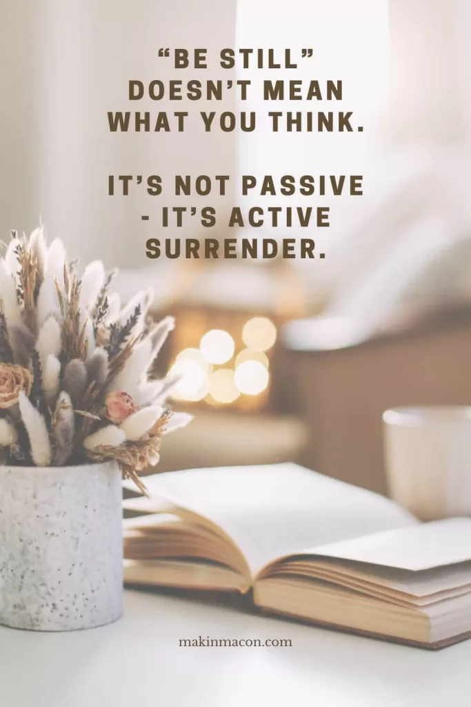 A cozy open book and dried flowers sit on a softly lit table with the quote “Be still doesn’t mean what you think. It’s not passive—it’s active surrender.”