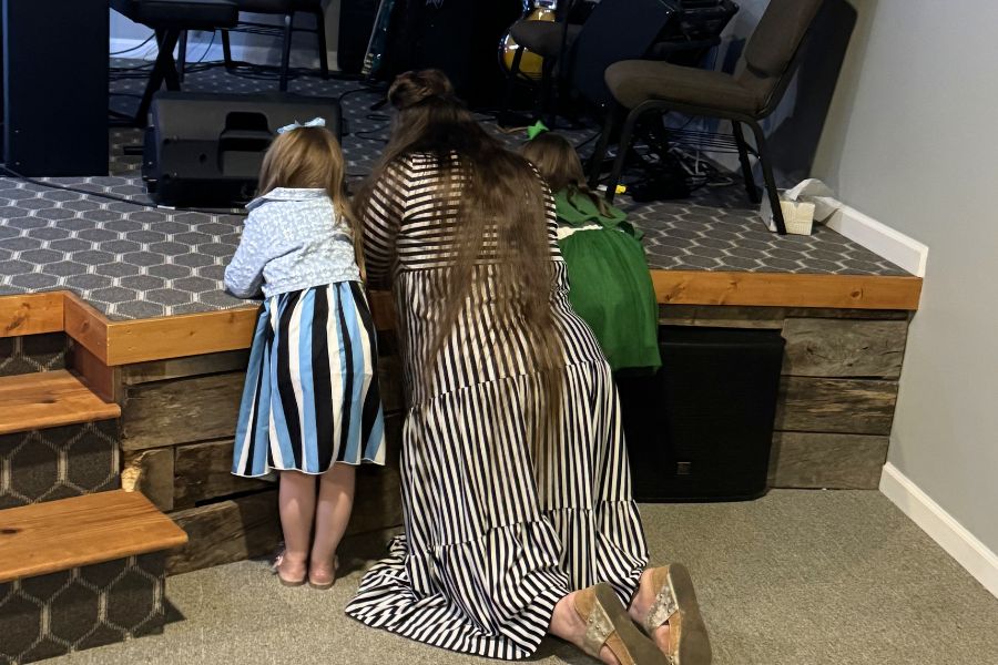 Mother kneeling with children at church altar teaching them how to pray, representing the quiet influence of a mother’s faith