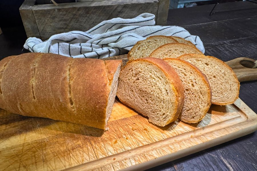 Fresh milled flour French bread sliced on a wooden cutting board showing soft interior and golden crust