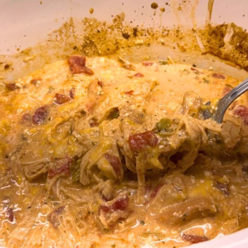 Creamy crockpot crack chicken made with shredded chicken, cream cheese, ranch seasoning, diced tomatoes, green chilies, bacon, and cheddar cheese, shown in a slow cooker with a spoon lifting a hearty serving.