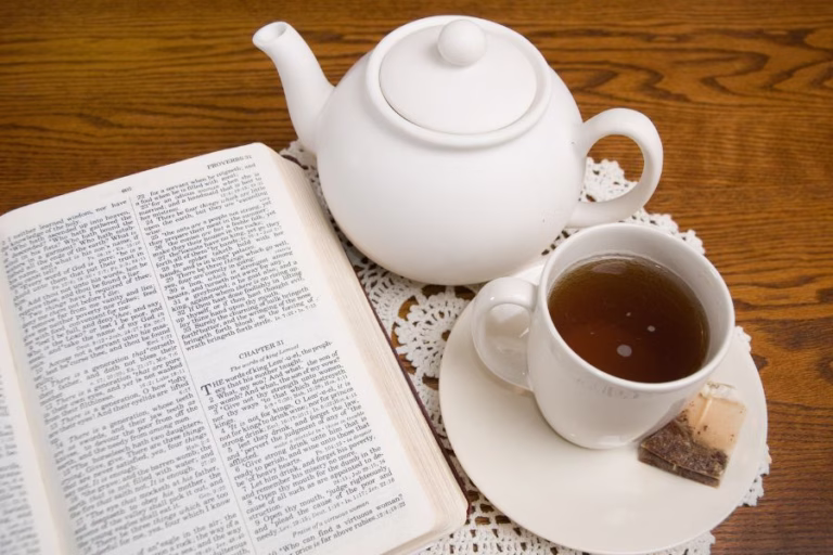 Open Bible beside a teacup and teapot on a wooden table, representing simple fall wellness habits, faith, rest, and seasonal homemaking routines.