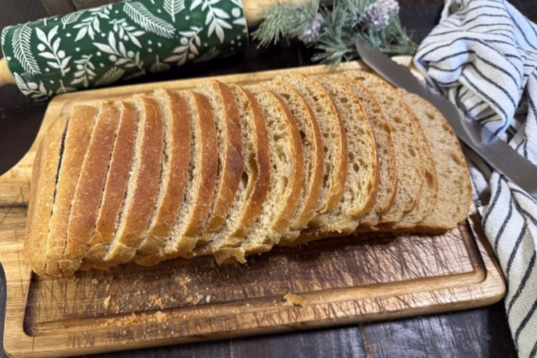 Fresh milled flour sourdough sandwich bread sliced on a wooden cutting board with a rolling pin and kitchen towel in the background.