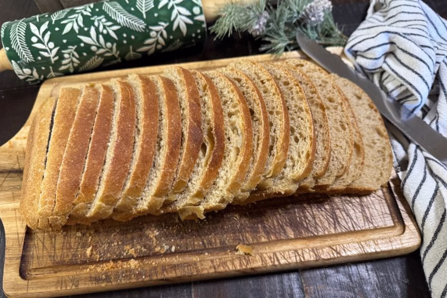 Fresh milled flour sourdough sandwich bread sliced on a wooden cutting board with a rolling pin and kitchen towel in the background.
