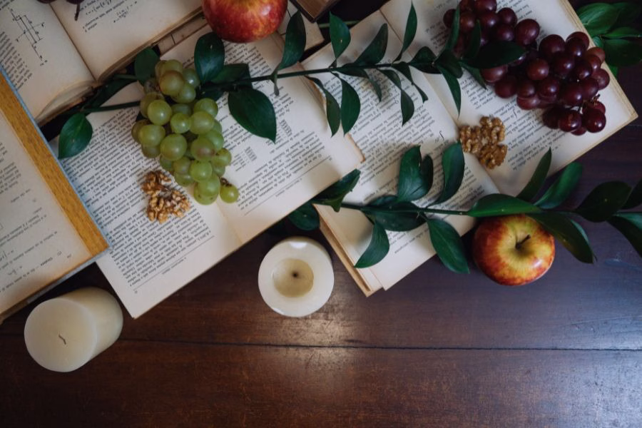Open pages with grapes, apples, greenery, walnuts, and candles arranged on a wooden table to represent the fruit of the Spirit and spiritual growth.